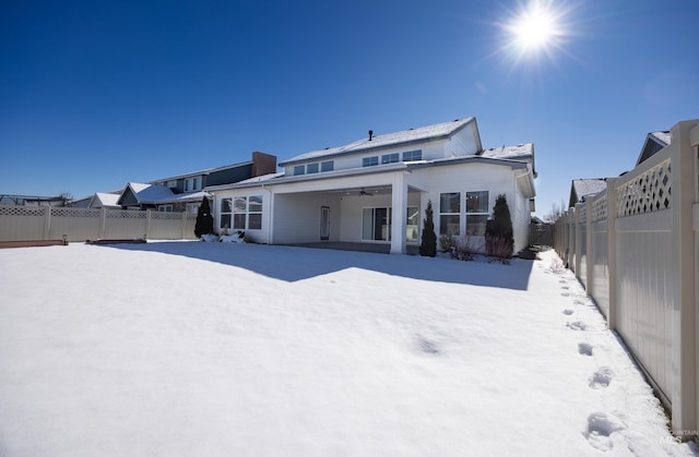 snow covered back of property featuring a fenced backyard and ceiling fan