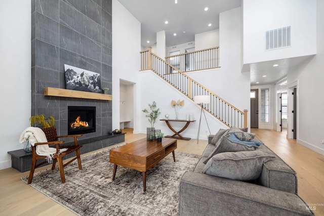 living area featuring visible vents, baseboards, stairs, a tile fireplace, and wood finished floors