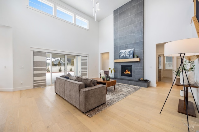 living area featuring a tiled fireplace, a towering ceiling, baseboards, and light wood finished floors