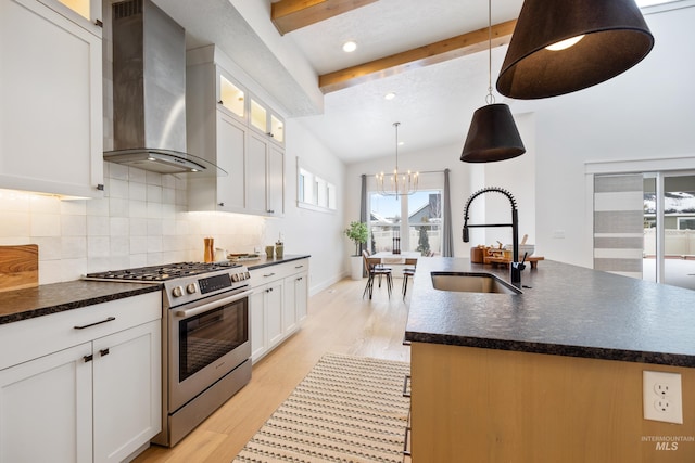 kitchen featuring light wood finished floors, stainless steel range with gas cooktop, a sink, decorative backsplash, and wall chimney range hood