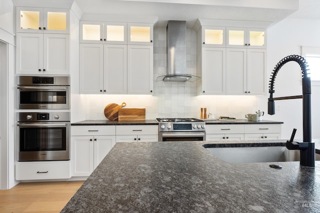 kitchen featuring a sink, stainless steel appliances, light wood-style floors, wall chimney exhaust hood, and decorative backsplash