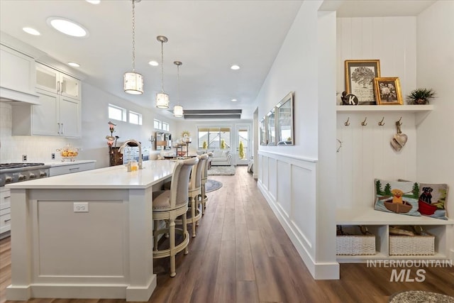 kitchen featuring glass insert cabinets, an island with sink, light countertops, decorative backsplash, and dark wood-style floors