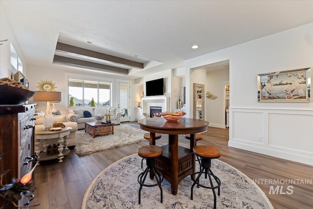 dining room with a decorative wall, a wainscoted wall, a glass covered fireplace, a raised ceiling, and wood-type flooring