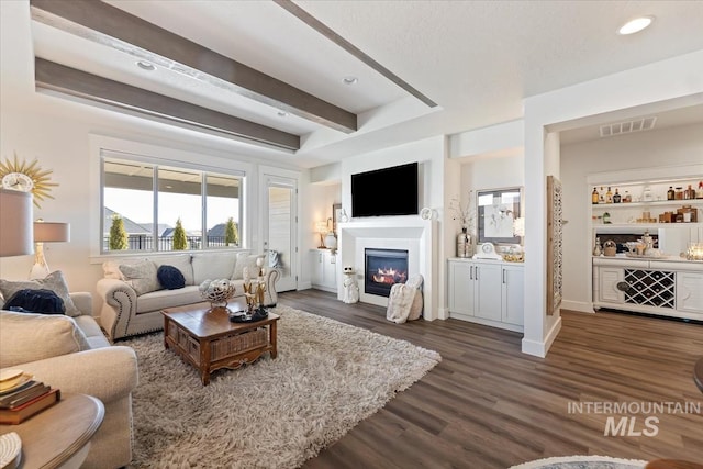 living room with visible vents, dark wood finished floors, recessed lighting, a glass covered fireplace, and beamed ceiling