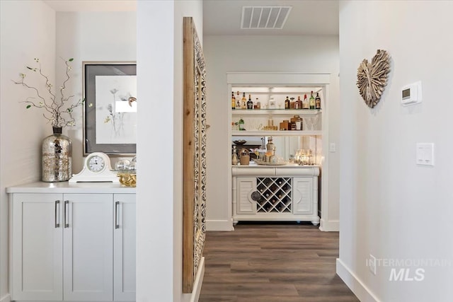 bar featuring visible vents, baseboards, a bar, and dark wood-style flooring