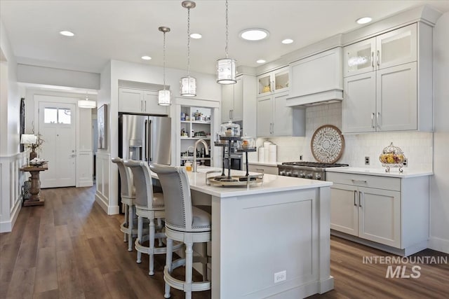 kitchen with pendant lighting, an island with sink, light countertops, custom exhaust hood, and stainless steel fridge