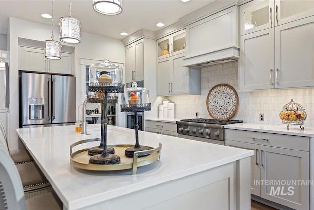 kitchen featuring a kitchen island with sink, stainless steel appliances, light countertops, custom range hood, and tasteful backsplash