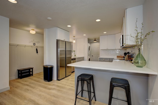 8561 W Goddard, Boise, ID 83704 - kitchen with light countertops, light wood-type flooring, stainless steel appliances, stacked washer and dryer, and a peninsula