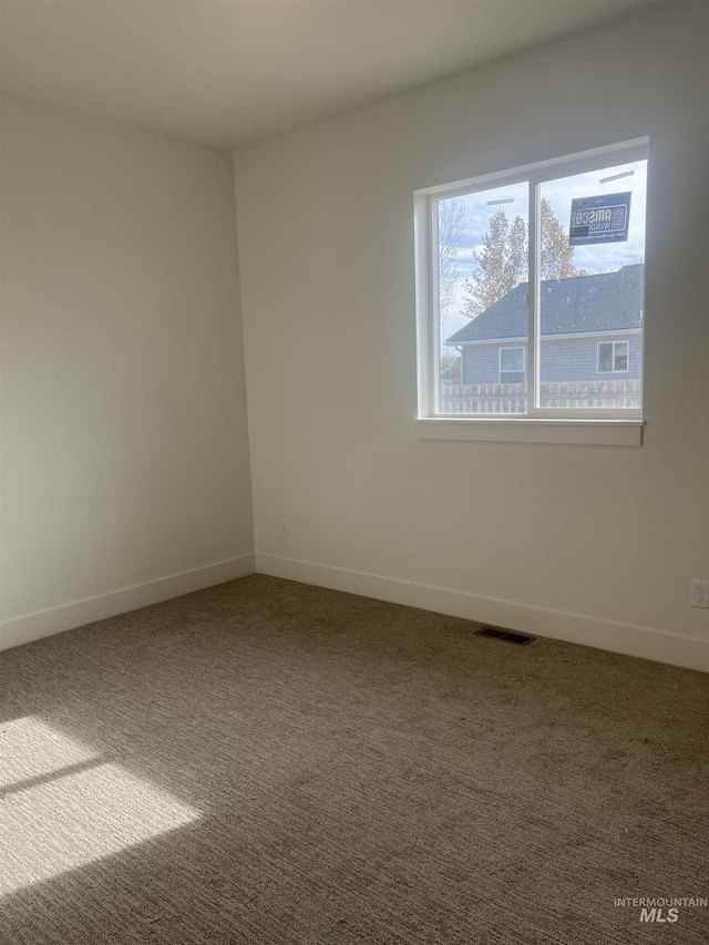 empty room featuring carpet floors, visible vents, and baseboards