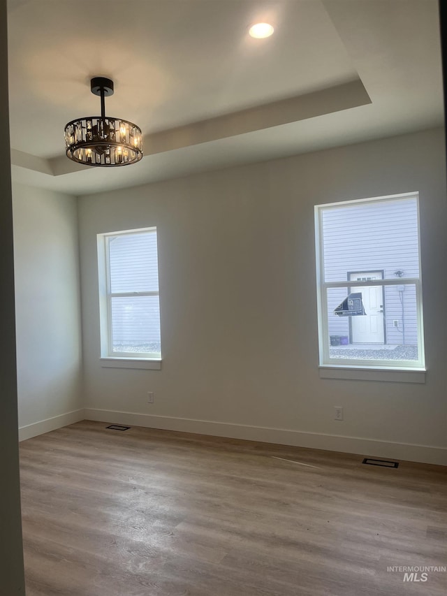 unfurnished room featuring a notable chandelier, wood finished floors, visible vents, and baseboards