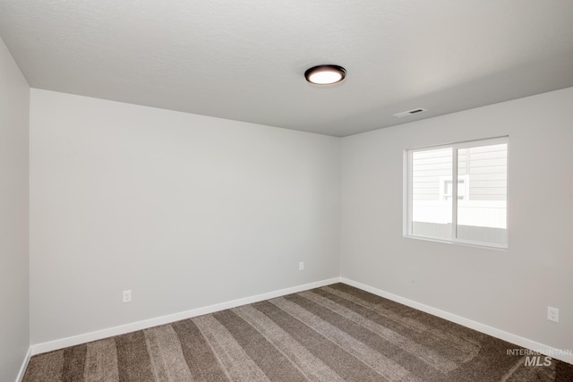 unfurnished room with dark carpet, visible vents, and baseboards