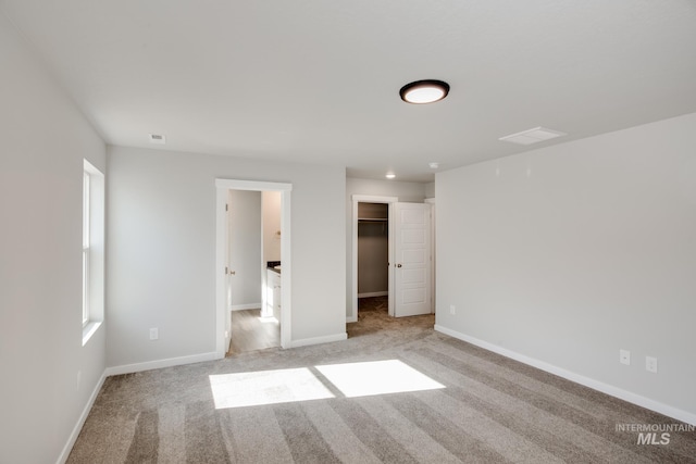 unfurnished bedroom featuring a walk in closet, light carpet, visible vents, and baseboards