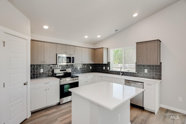 kitchen with appliances with stainless steel finishes, vaulted ceiling, light wood finished floors, and tasteful backsplash