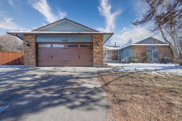 ranch-style house with driveway, stone siding, an attached garage, and fence