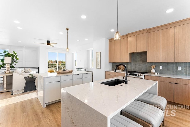 kitchen featuring a sink, a kitchen island with sink, gas range oven, light wood-style floors, and recessed lighting