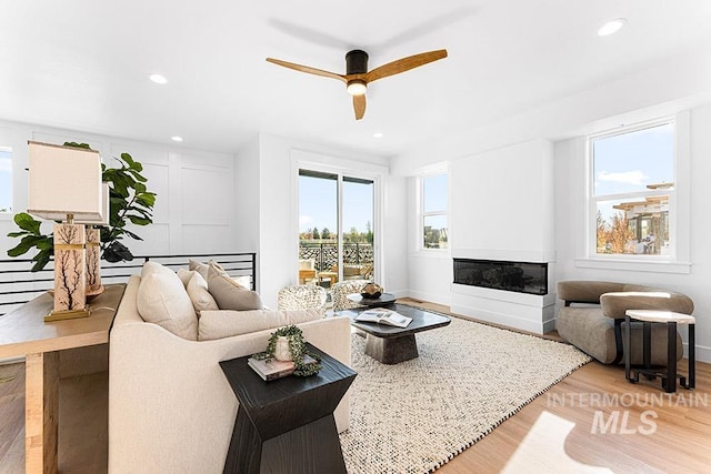 living area featuring light wood-style floors, ceiling fan, recessed lighting, a glass covered fireplace, and baseboards