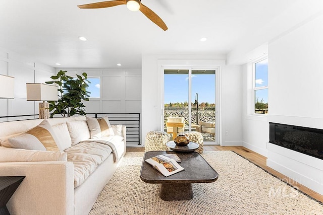 living area featuring wood finished floors, ceiling fan, recessed lighting, baseboards, and a glass covered fireplace