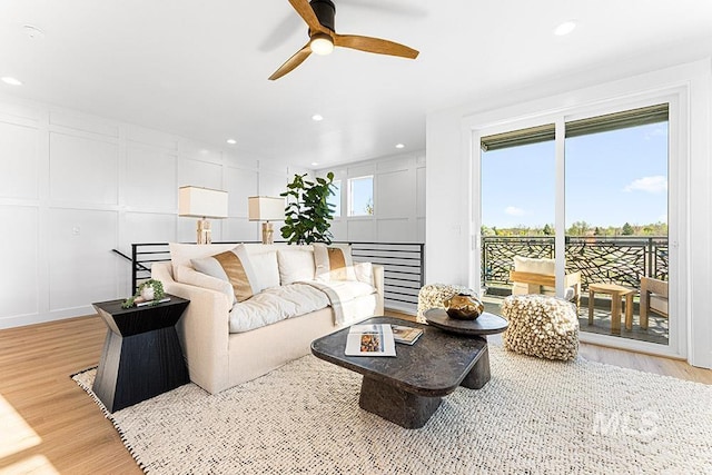 living area with light wood finished floors, a ceiling fan, a decorative wall, and recessed lighting