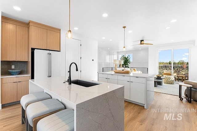 kitchen with high end fridge, an island with sink, a sink, light wood-style flooring, and recessed lighting