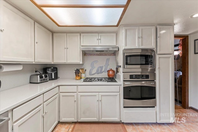 kitchen featuring light countertops, white cabinets, under cabinet range hood, stainless steel appliances, and light tile patterned flooring
