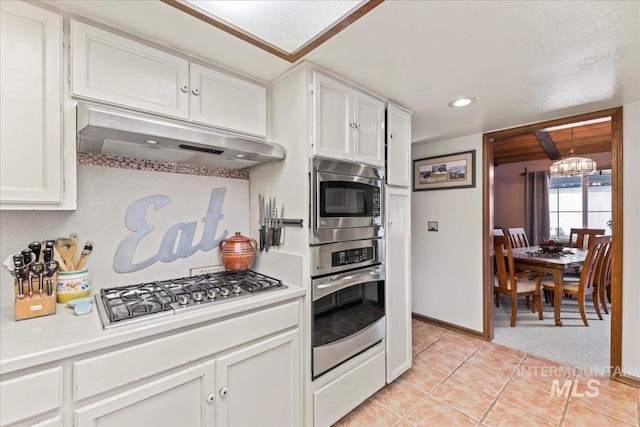 kitchen featuring light tile patterned flooring, light countertops, under cabinet range hood, appliances with stainless steel finishes, and a notable chandelier