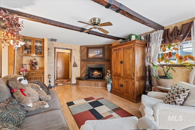 living area with visible vents, beam ceiling, a fireplace, ceiling fan, and light wood finished floors