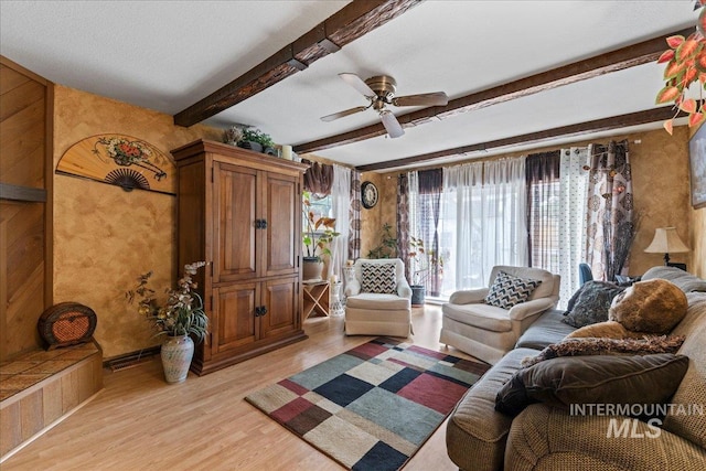 living room featuring beamed ceiling, ceiling fan, wallpapered walls, and light wood-style floors