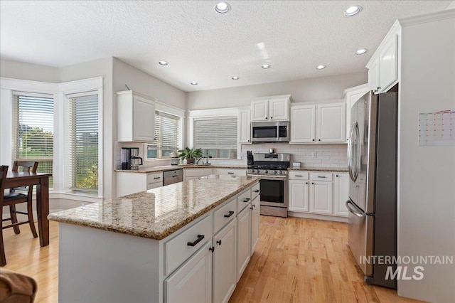 kitchen featuring decorative backsplash, light stone countertops, stainless steel appliances, white cabinets, and a center island