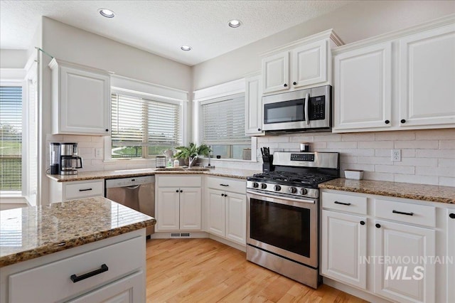 kitchen featuring light stone countertops, decorative backsplash, stainless steel appliances, and white cabinetry