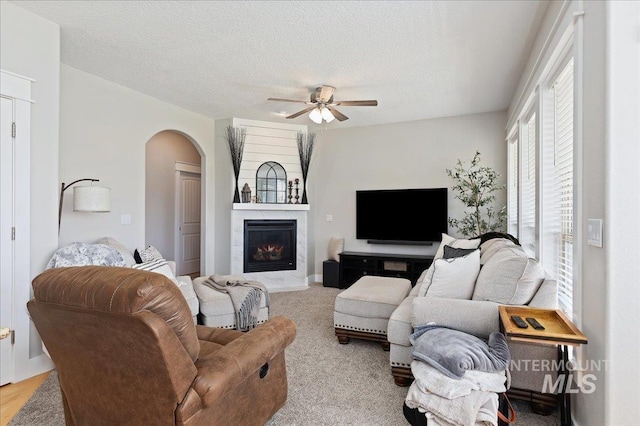 carpeted living room featuring a textured ceiling, a large fireplace, and ceiling fan