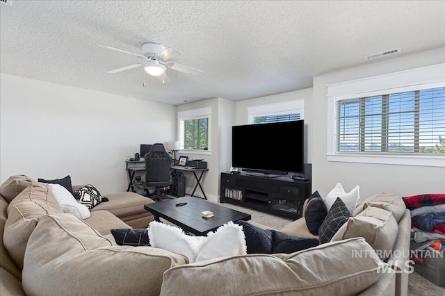 carpeted living room with a wealth of natural light, ceiling fan, and a textured ceiling