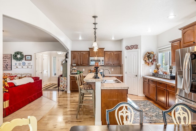 kitchen with backsplash, stainless steel appliances, sink, pendant lighting, and a center island with sink