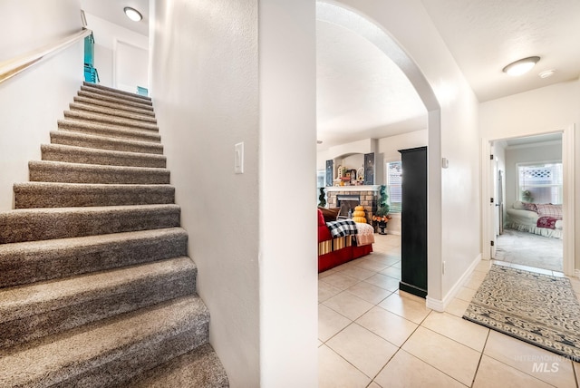 stairs with tile patterned floors and a brick fireplace