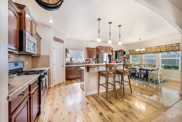 kitchen with a center island, an inviting chandelier, backsplash, pendant lighting, and appliances with stainless steel finishes