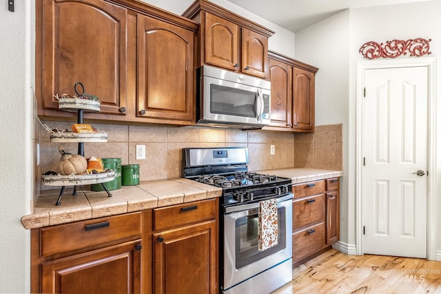 kitchen featuring backsplash, tile counters, light hardwood / wood-style floors, and stainless steel appliances