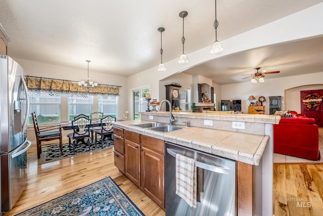 kitchen featuring appliances with stainless steel finishes, ceiling fan with notable chandelier, sink, a center island with sink, and decorative light fixtures