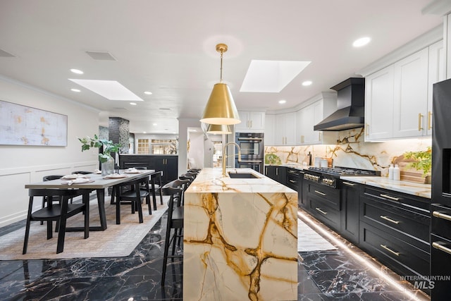 kitchen with wall chimney exhaust hood, dark cabinetry, a skylight, and white cabinets