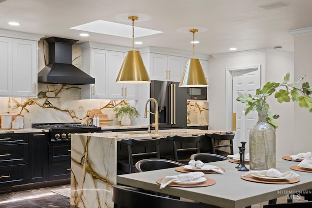 kitchen with decorative light fixtures, white cabinets, high quality fridge, wall chimney range hood, and an island with sink