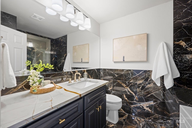 full bath with visible vents, toilet, marble finish floor, vanity, and tile walls