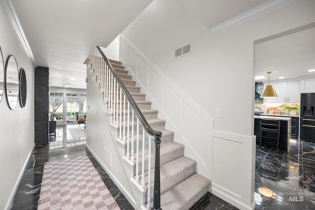 staircase featuring visible vents, a wainscoted wall, ornamental molding, marble finish floor, and a decorative wall