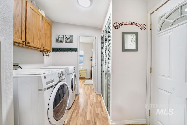 washroom featuring cabinets, washing machine and dryer, and light wood-type flooring