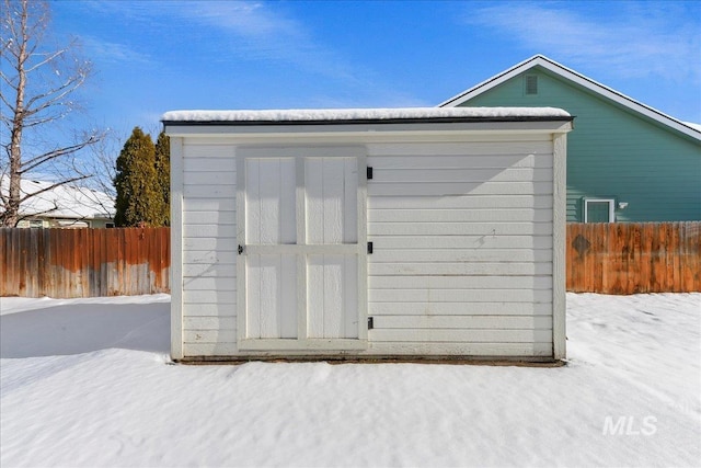 snow covered structure featuring an outbuilding, a storage shed, and fence