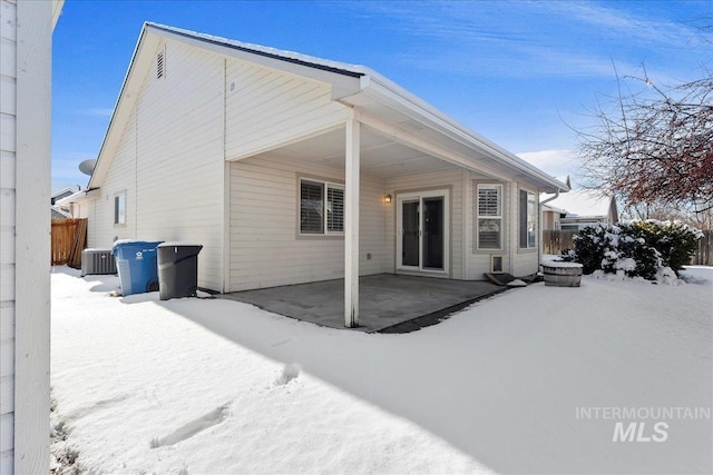 snow covered house with a patio, central AC unit, and fence