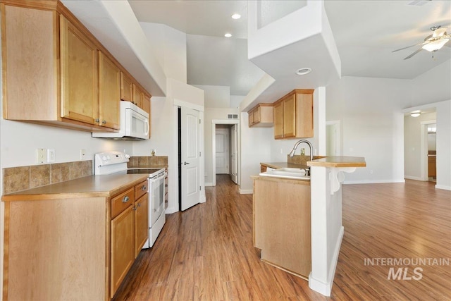 kitchen featuring a peninsula, white appliances, a sink, and light wood-style flooring