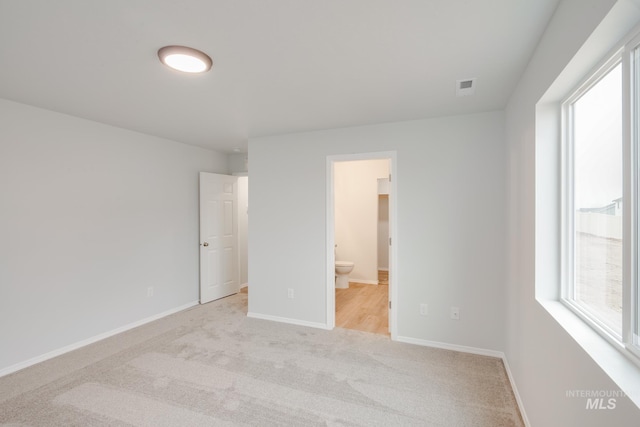 unfurnished bedroom featuring light colored carpet and connected bathroom