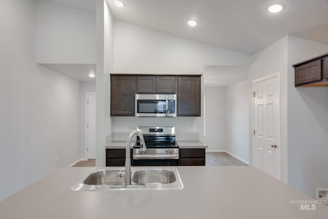 kitchen featuring lofted ceiling, sink, dark brown cabinets, stainless steel appliances, and light hardwood / wood-style floors