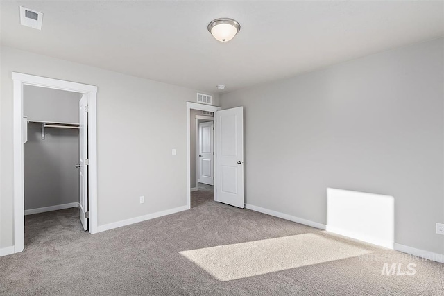 unfurnished bedroom with a walk in closet, a closet, and light colored carpet