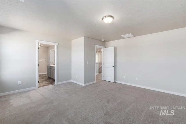 unfurnished bedroom with a spacious closet, a textured ceiling, light carpet, and connected bathroom