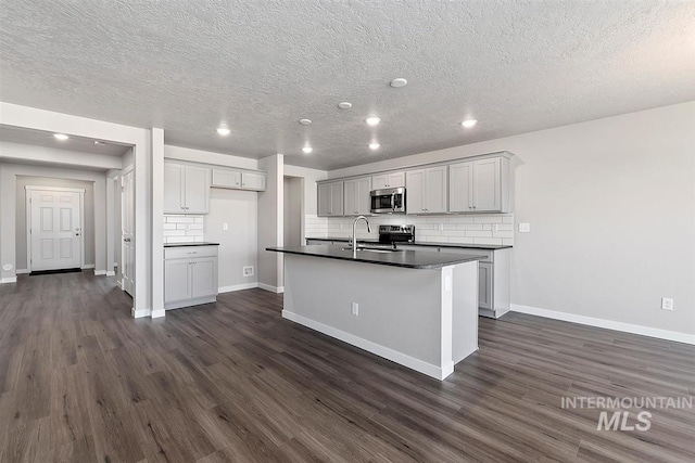 kitchen with dark hardwood / wood-style floors, decorative backsplash, sink, a kitchen island with sink, and gray cabinetry