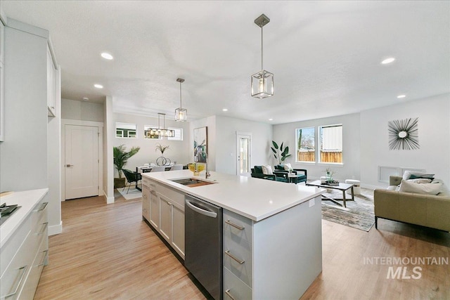 kitchen featuring light wood-type flooring, stainless steel dishwasher, a center island with sink, white cabinetry, and hanging light fixtures